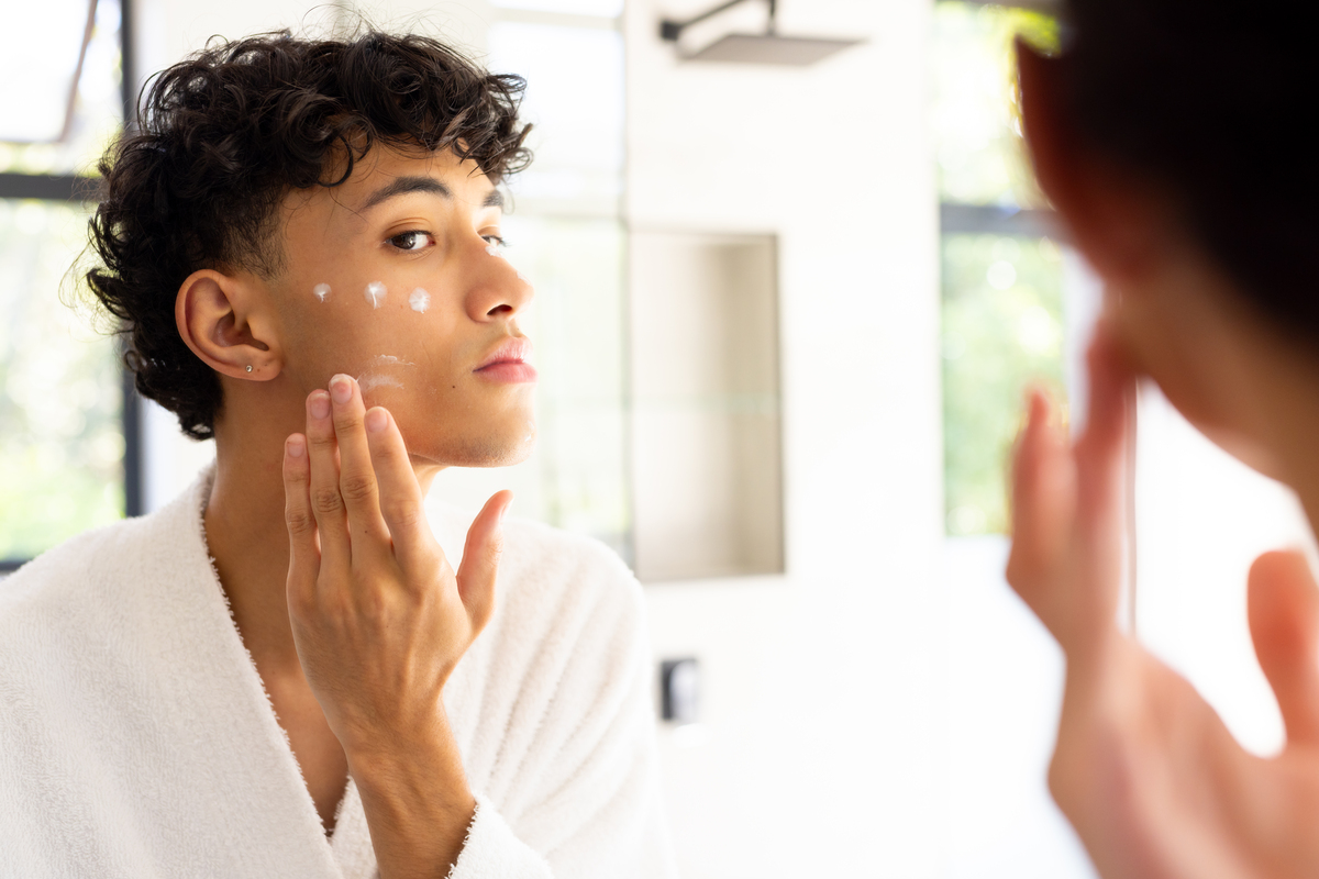 young man applying skincare in the mirror